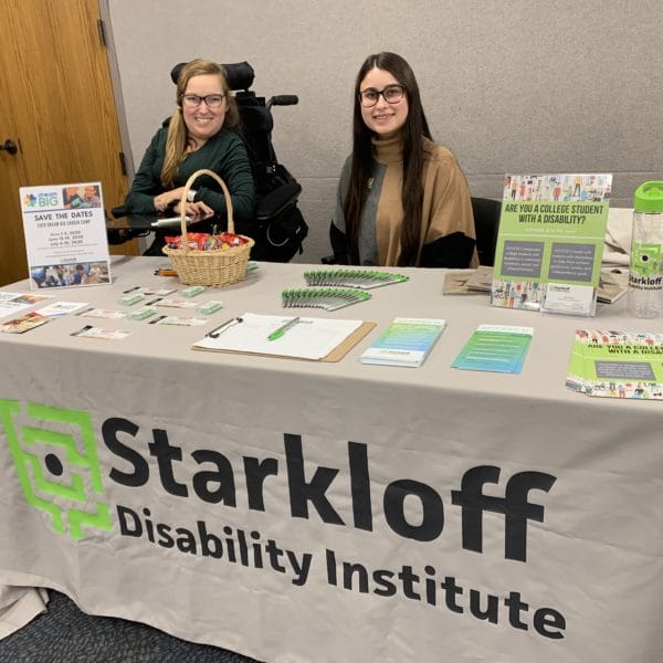 Sarah Schwegel and Katie Fields sit at a table with Starkloff Disability Institute's logo displayed on the table cloth.