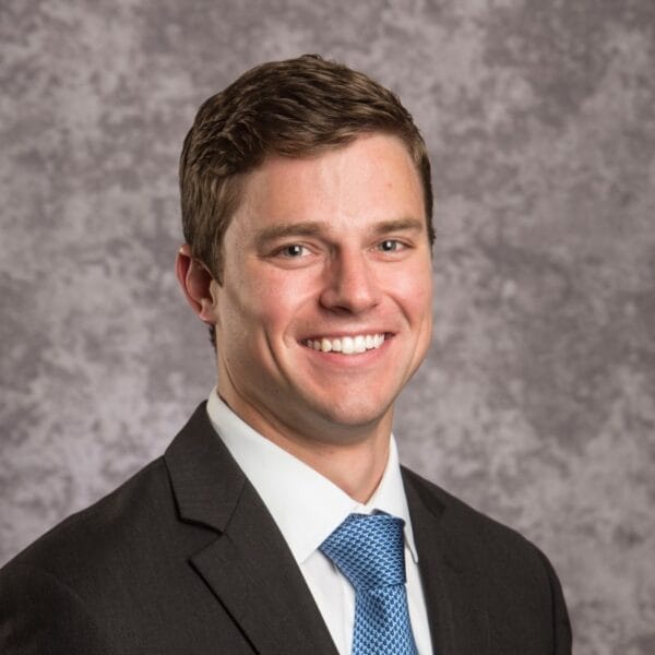 Kevin Erbs smiles at the camera. Kevin has peach skin, brown hair and is wearing a suit with a light teal tie.