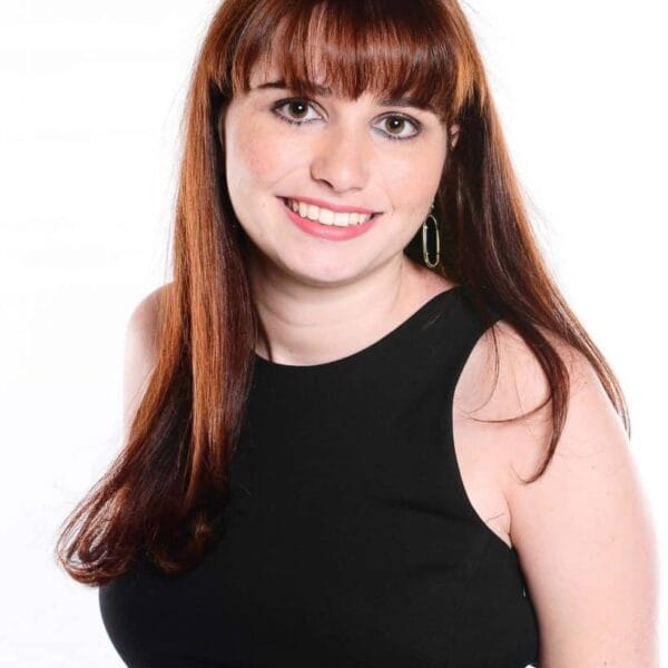 Haley is smiling over her shoulder for a headshot. She has red hair with bangs and is wearing a black top.