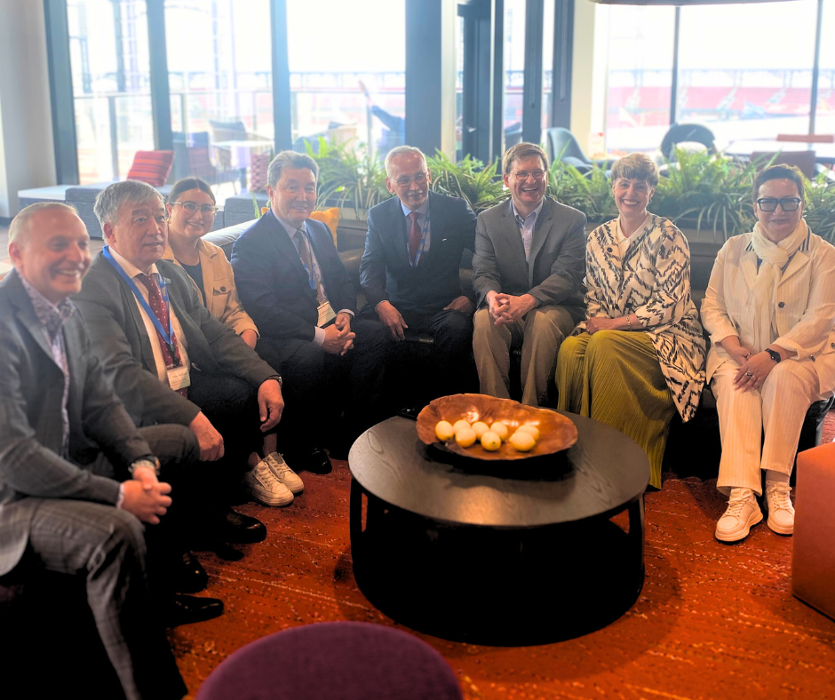 Eight adults in business attire sit on a L-shaped couch smiling.