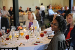 People seated at a luncheon in a large room listening to remarks delivered by someone out of the frame.