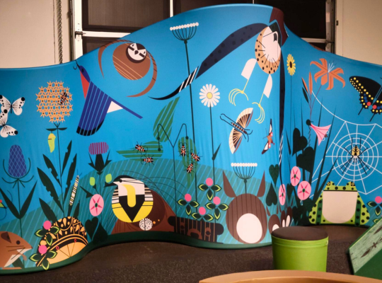 3 – I am wild exhibit wall – Pittsburgh Children’s Museum A blue panel with drawings of birds and flowers from "i am wild: a charley harper exhibit."