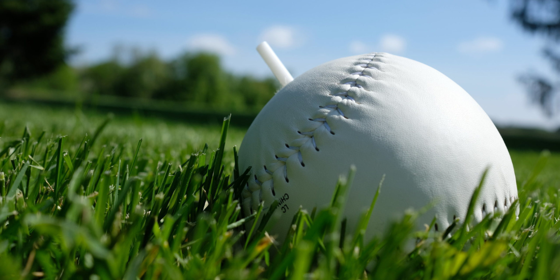 BeepBall header photo from MindsEye A beep baseball sitting in the grass. It is a bit larger than a softball and has a plastic post sticking out of the top.