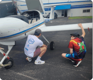 A student looks at the wheel of a small plane with an instructor.
