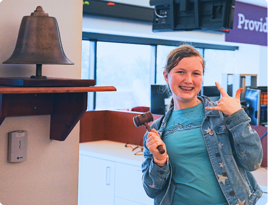 2025-camp-report-wfbell s: 1. Students playing a group game with a large ball of yarn crisscrossed between them. 2. A student next to the closing bell at Wells Fargo with ASL sign for I love you.