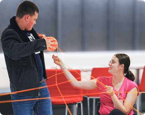 2025-camp-report-yarn-activity Students playing a group game with a large ball of yarn crisscrossed between them.