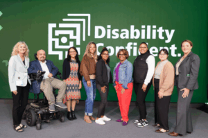 Group of Starkloff staff, board members, and attendees smiling onstage. The background is Starkloff’s Disability Confident logo.
