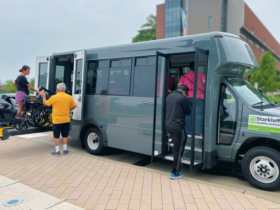 People boarding a small bus, including using a wheelchair lift.