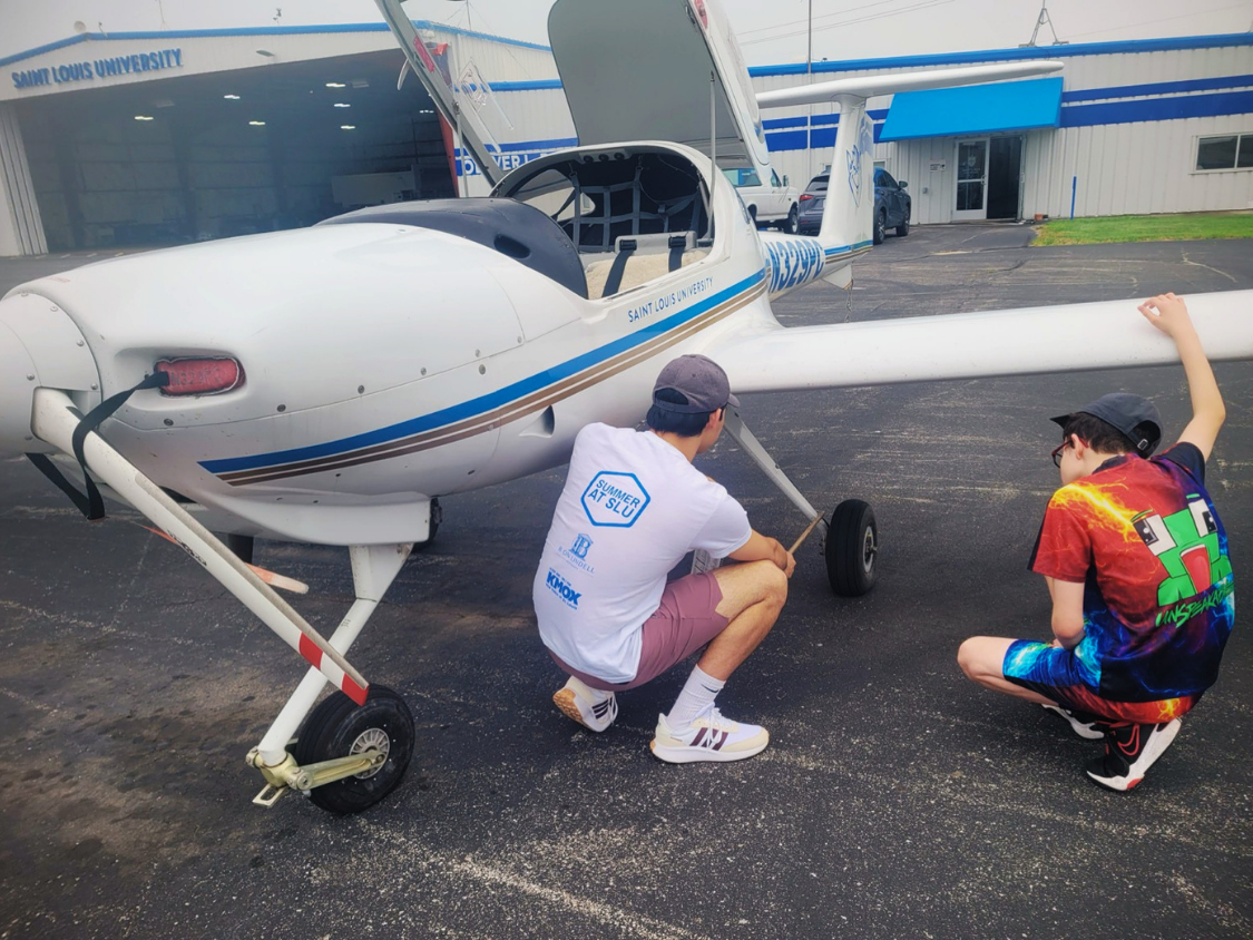 A SLU student and a Dream Big participant looking at the landing gear of a small prop plane.