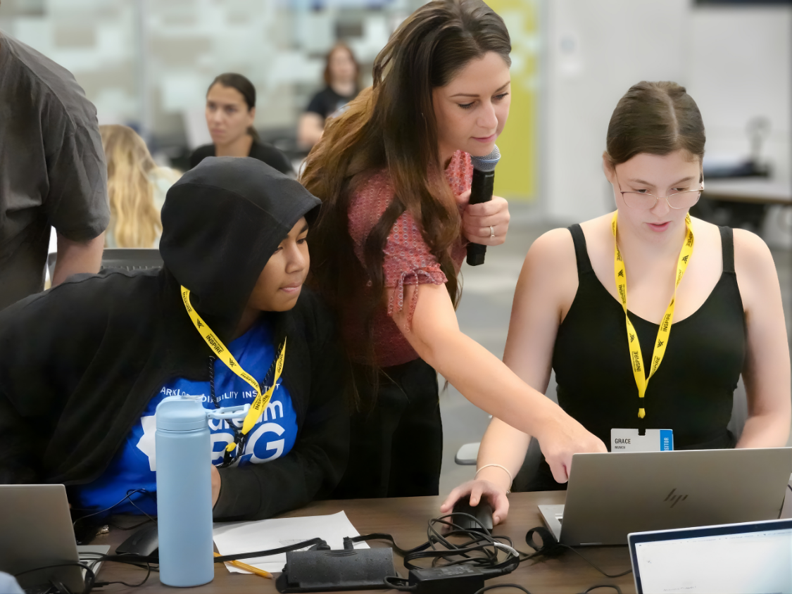 Dream Big Camp visit to World Wide Technology, an employee helps students using laptops during project.