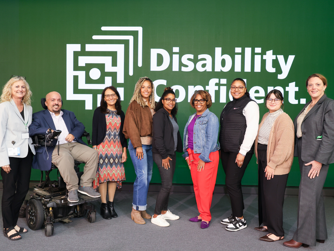 Group of Starkloff staff, board members, and attendees smiling onstage. The background is Starkloff’s Disability Confident logo.
