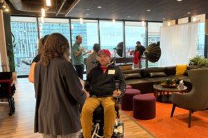 Several young professionals chat in an office lounge area, with a photographer set up in the background.