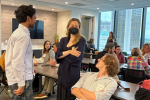 Several young professionals chat in a conference room, some are wearing masks.