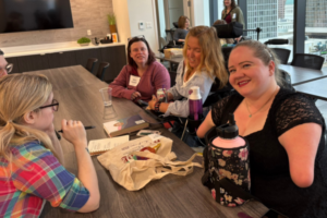 Four young woman chat at a table together, some with obvious disabilities.