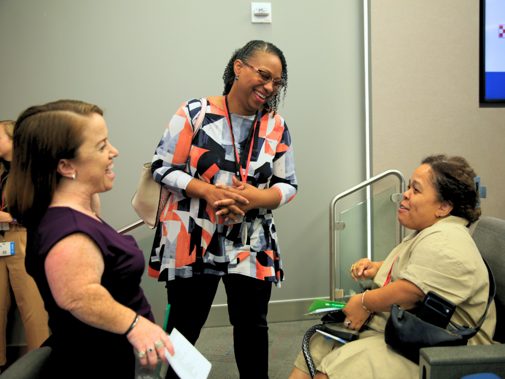 Three women laugh together. Two are little people and the other is average height.