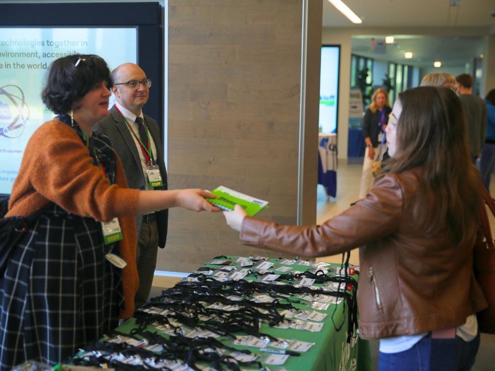 Person checks into the conference, greeted by smiling staff and grabbing Disability Confident swag.