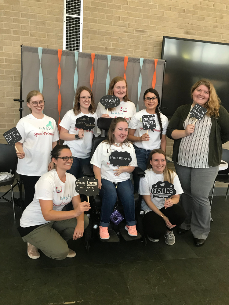 College disability organization Eight young women smile together, holding small, handmade signs celebrating disability inclusion.