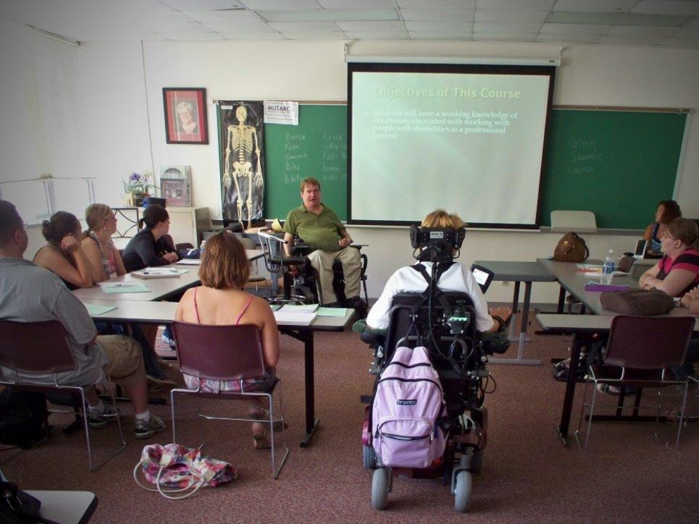 Steve teaching Steve Foelsch, a power wheelchair user, teaching in a college classroom.