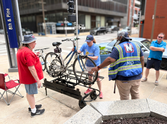 Lori secures her bike's front wheel on the practice rack with three Metro employees to offer guidance.