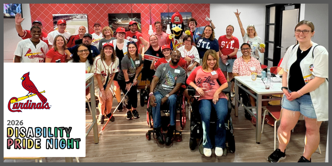 Cardinals 2026 Disability Pride Night. About 25 adults in Cardinals Disability Pride shirts in a suite with Fredbird at Busch Stadium, all beaming at the camera. The group includes disabled and nondisabled people, apparent disabilities include manual and power wheelchair users, a person with limb difference, and a person holding a white cane. Everyone is having a great time!