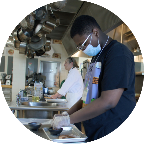 Culinary Arts at St. Louis Community College. Student wearing gloves seasons chicken in an industrial kitchen.
