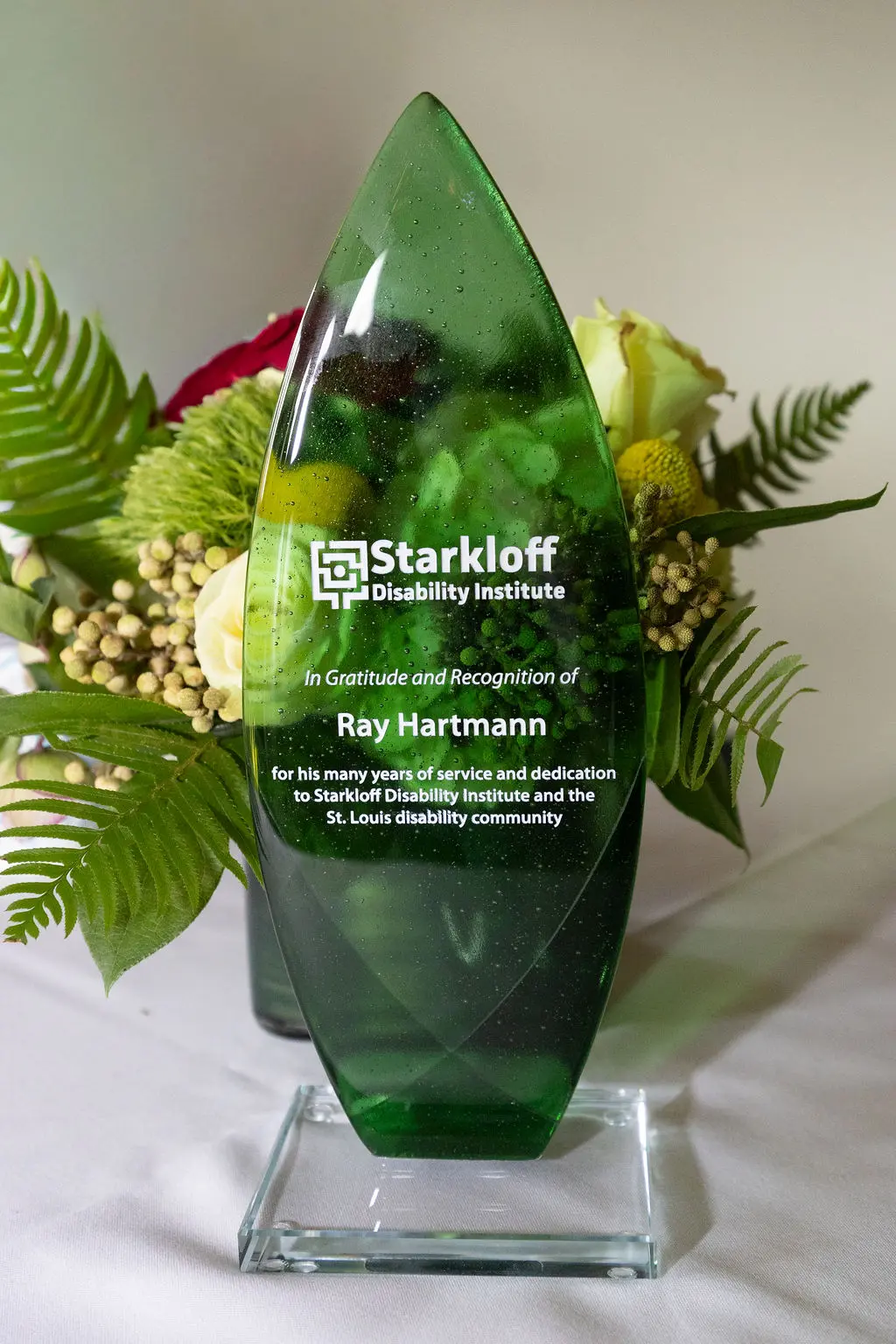 Award made of green glass reads: In gratitude and recognition of Ray Hartmann for his many years of service and dedication to Starkloff Disability Institute and the St. Louis disability community. Starkloff Disability Institute.